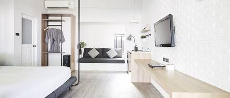 A modern hotel room with a bed, a seating area with a sofa, a TV mounted on the wall, and a wooden desk.