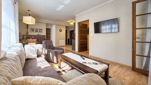 A living room with a sofa, armchair, and coffee table, a TV mounted on the wall, and a wooden floor. - SKY Apartments VisitZakopane (Zakopane)