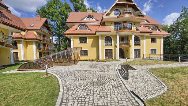 A large yellow building with multiple balconies and a cobblestone driveway. - SKY Apartments VisitZakopane (Zakopane)