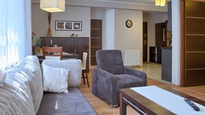 A modern living room with a sofa, armchair, and dining table. There is a kitchen area visible in the background. - SKY Apartments VisitZakopane (Zakopane)