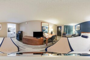 Habitación de hotel con cama, escritorio, silla, televisor y vista al pasillo.