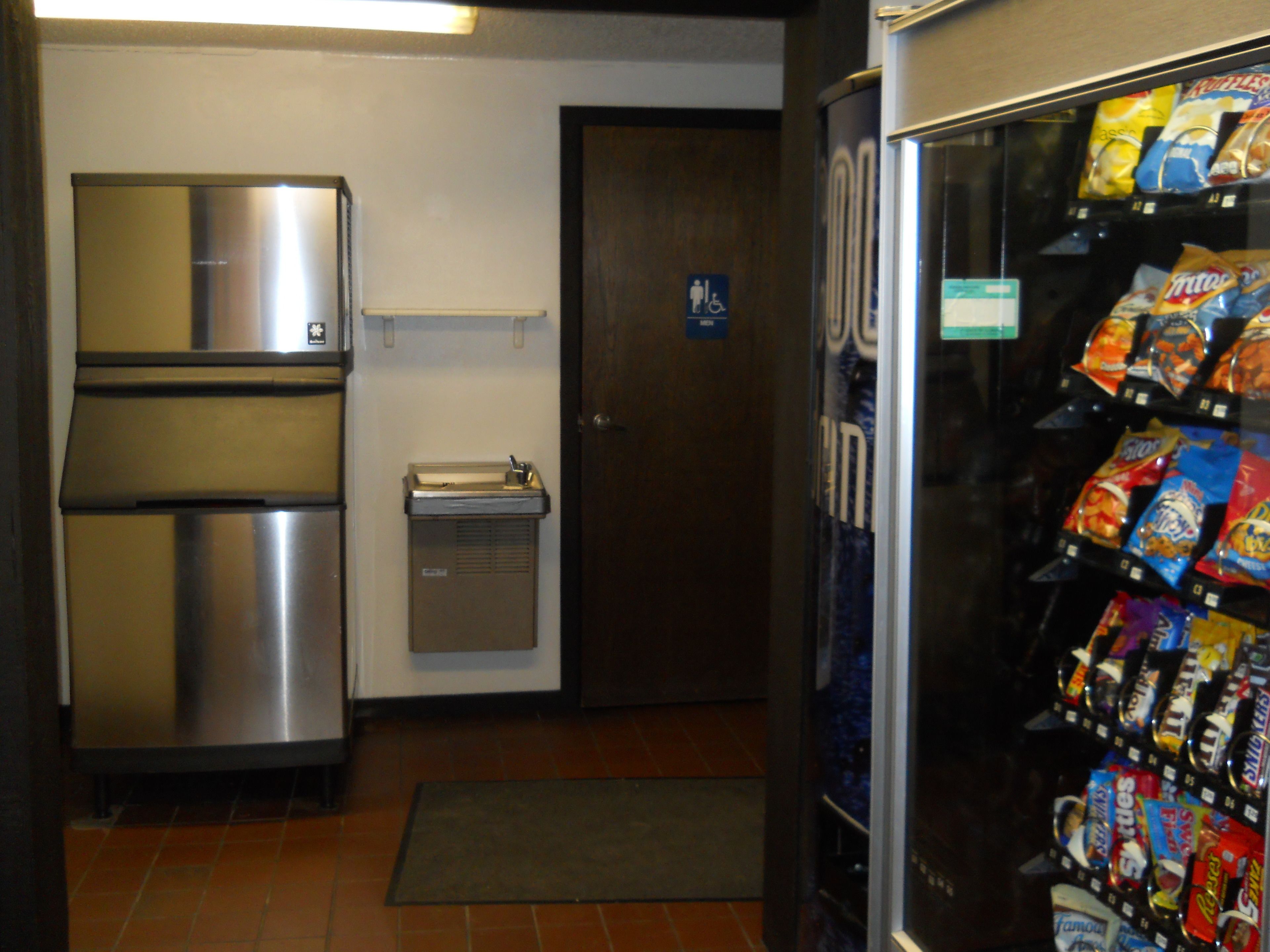 A vending machine stocked with snacks, a stainless steel refrigerator, and a small sink.