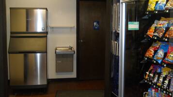 A vending machine stocked with snacks, a stainless steel refrigerator, and a small sink.