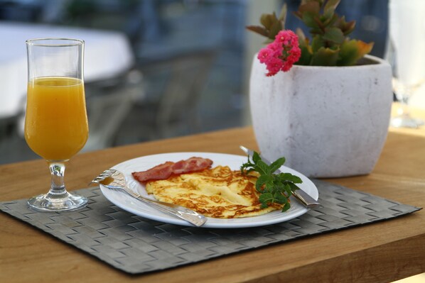 A breakfast plate with eggs, bacon, and a glass of orange juice on a woven placemat. - Chios Xenia Studio & Apartments (Chios)