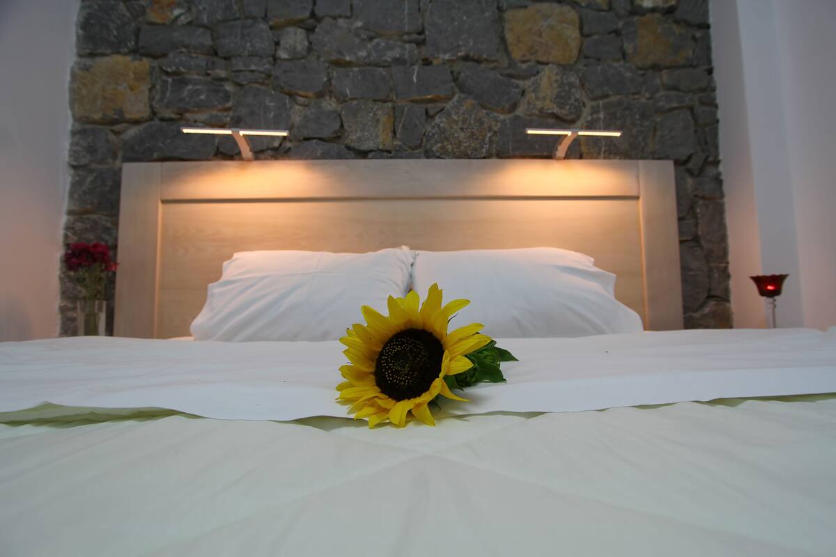 Una cama con ropa blanca, una decoración de girasol y una pared de piedra de fondo.