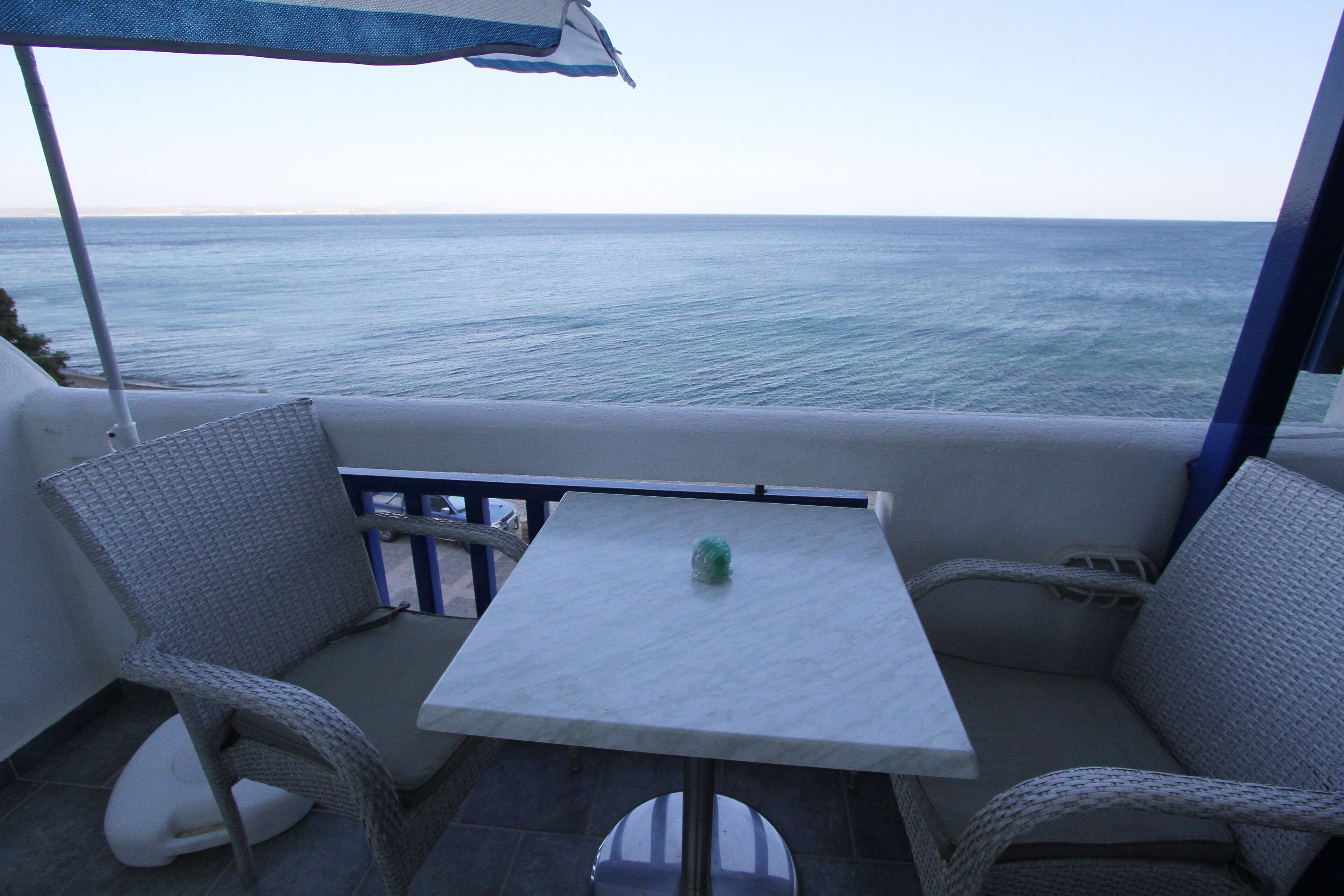 Un balcon avec des fauteuils en osier, une petite table et une vue sur la mer.