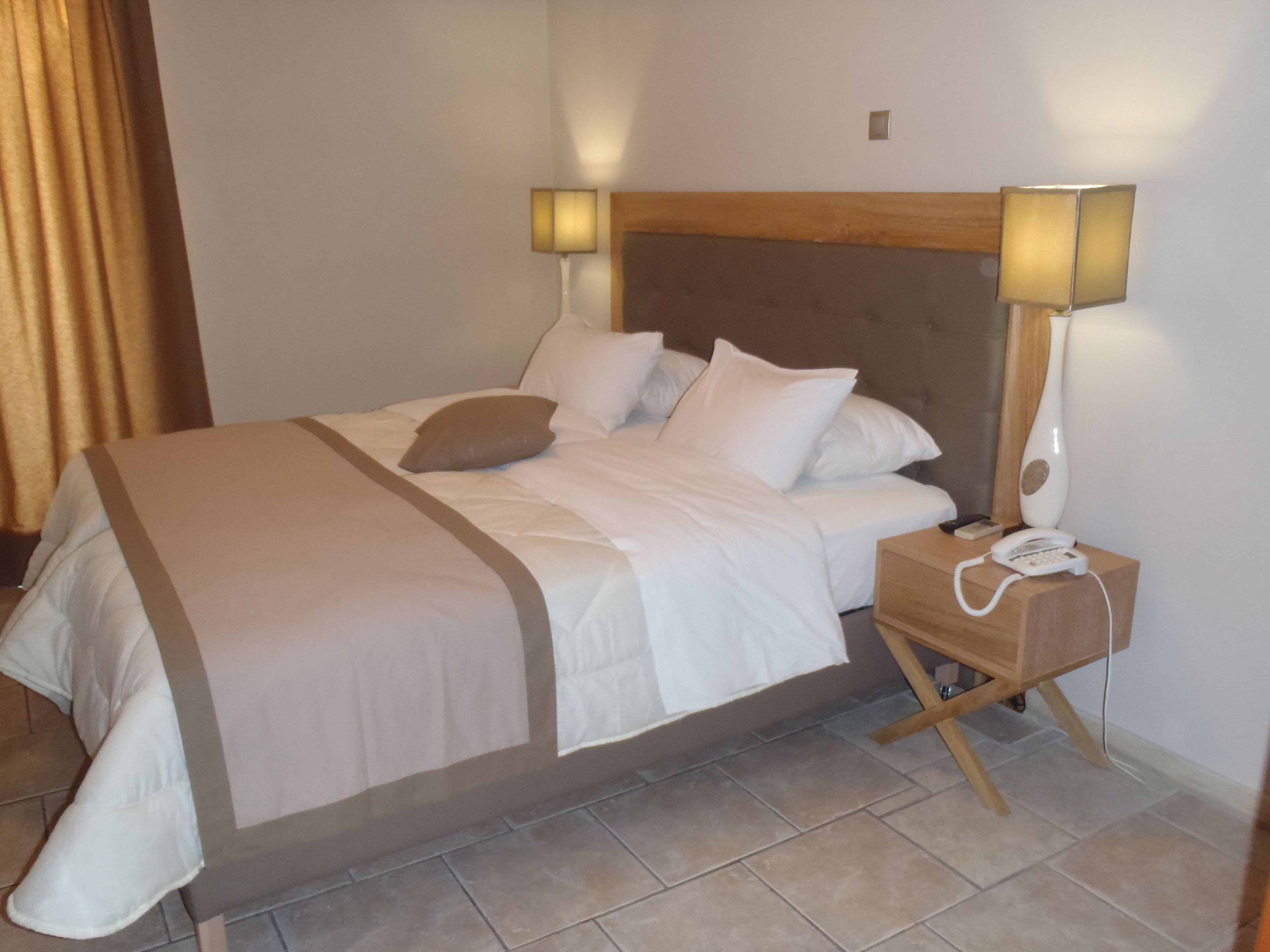 A neatly made bed with white linens and a beige throw blanket, a bedside table with a lamp and a phone, and a wooden headboard.