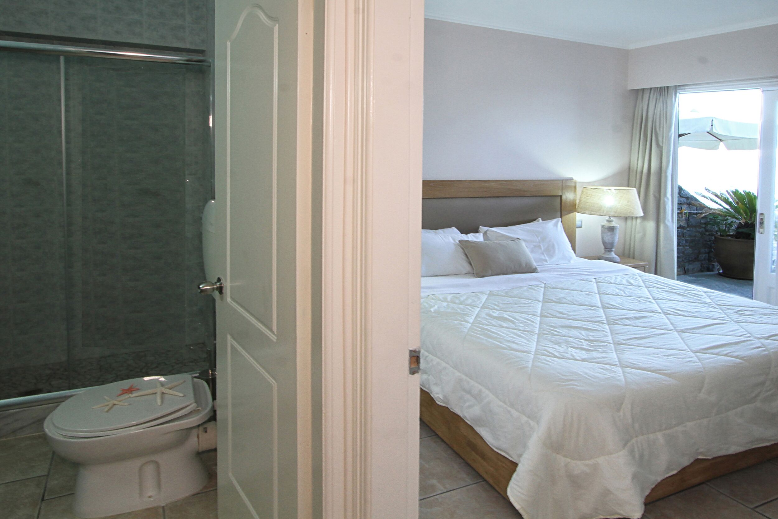 Una habitación de hotel con cama, lámpara de noche y baño con inodoro y ducha.