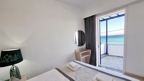 A hotel room with a bed, a bedside table with a lamp, a mirror, and a view of the ocean through a sliding door. - Chios Xenia Studio & Apartments (Chios)