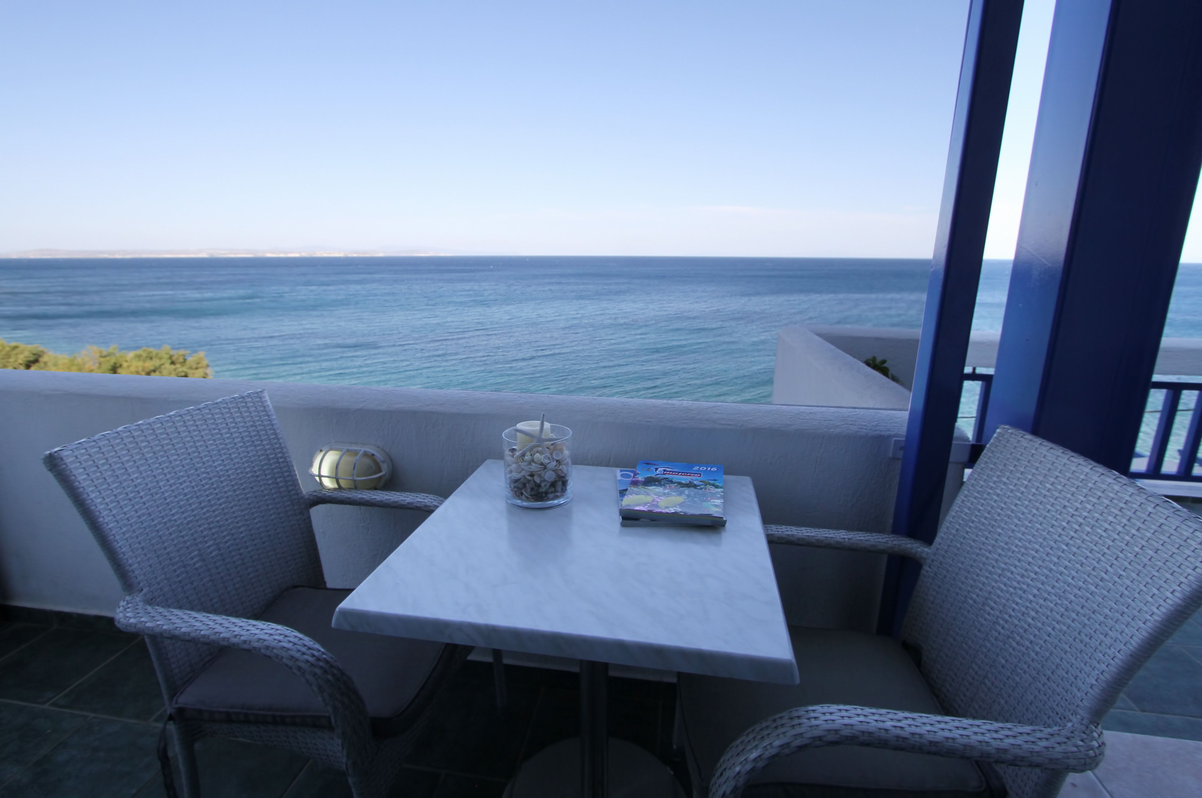 A balcony with wicker chairs and a table, overlooking the sea.