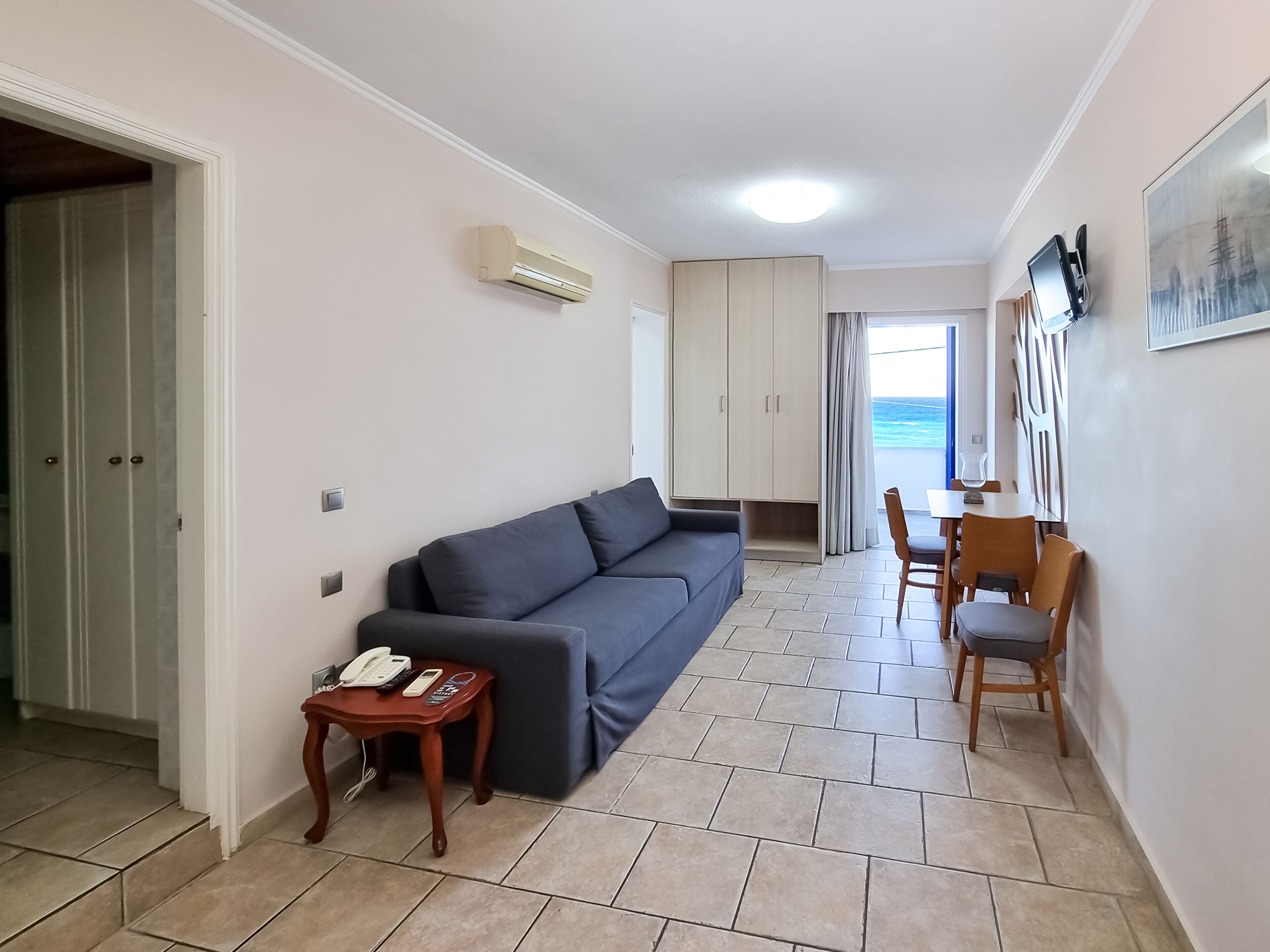 Un espacio habitable compacto con un sofá, una mesita con teléfono, una zona de comedor con sillas y vistas al océano a través de una ventana.