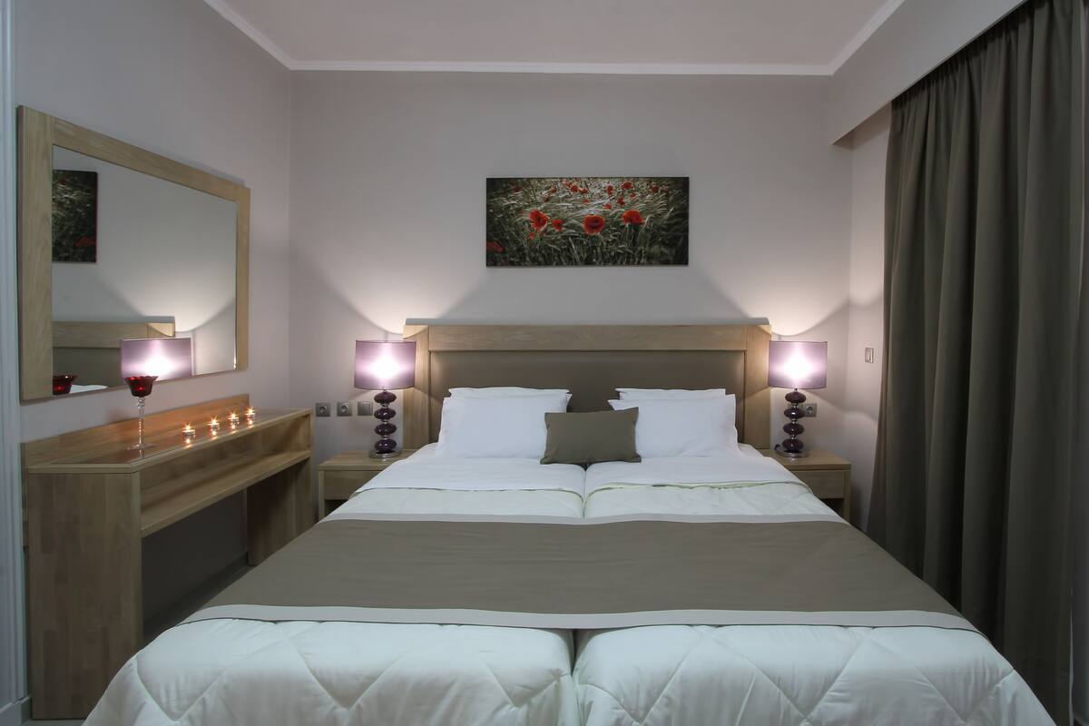 Habitación de hotel con una cama grande, dos mesitas de noche con lámparas, un espejo y un cuadro en la pared.