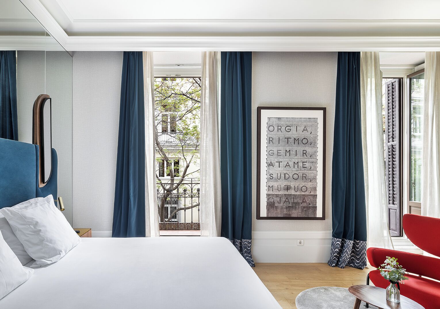 Une chambre d’hôtel moderne avec un grand lit, un fauteuil rouge et une citation encadrée accrochée au mur.