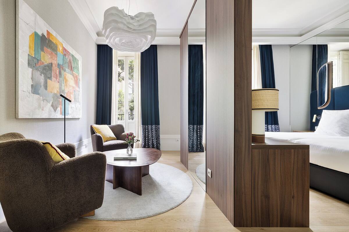 Een moderne hotelkamer met een ronde salontafel, een bank, een bed en een groot abstract schilderij aan de muur.