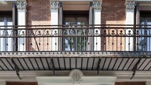 A building with a brick facade, a balcony with wrought iron railings, and a glass entrance door. - One Shot Recoletos (Madrid)