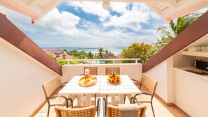 Un balcon avec une table dressée pour deux personnes, un panier de fruits et un grand verre à bière.