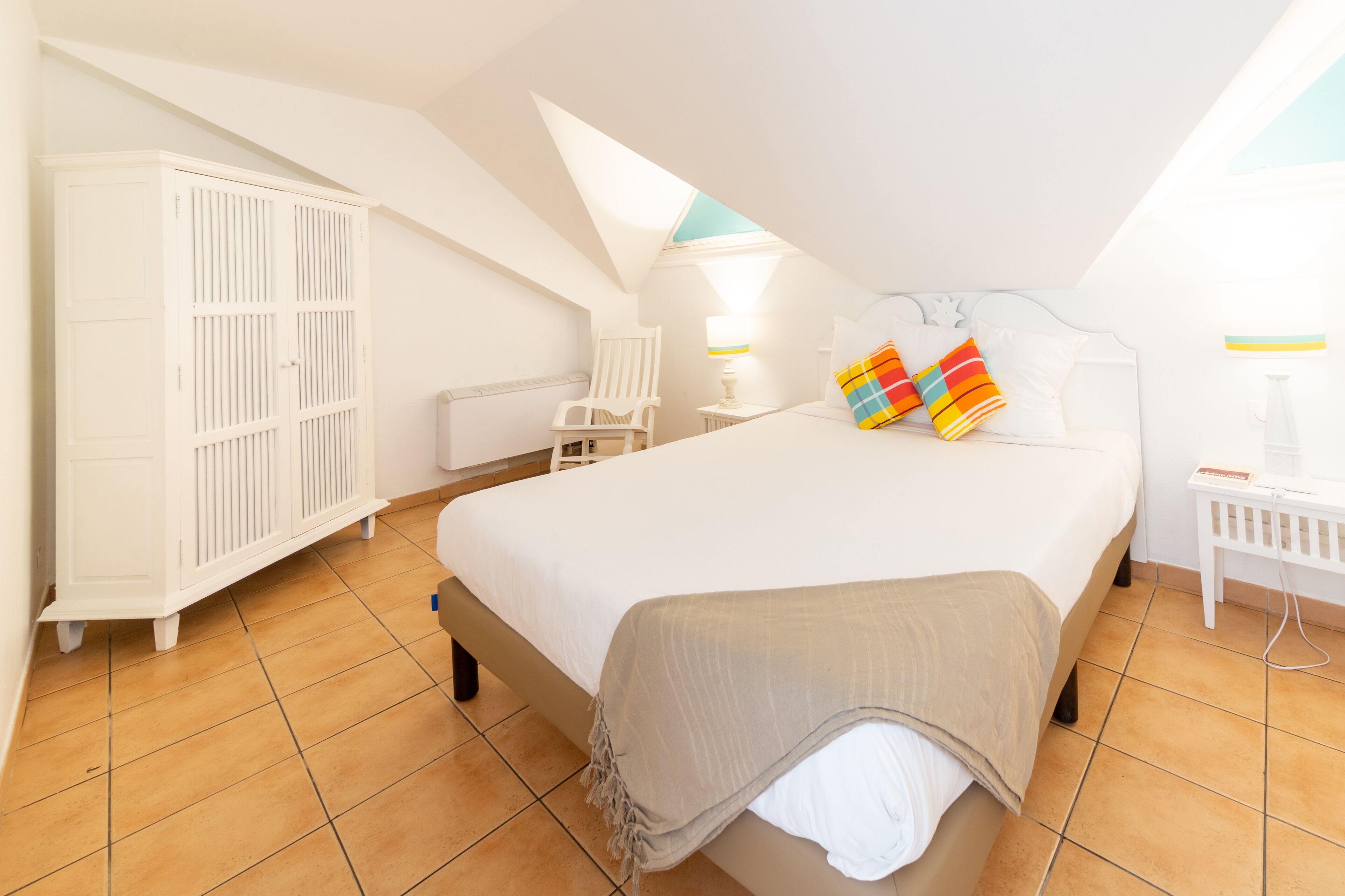 Un dormitorio con una cama grande, un armario, una silla y una mesita de noche con una lámpara.
