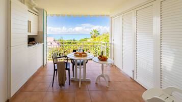 A balcony with a table and chairs, a small table with fruit, and a view of the ocean.