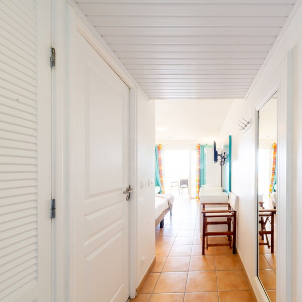 A hallway with a bed, a chair, and a bathroom with a mirror.