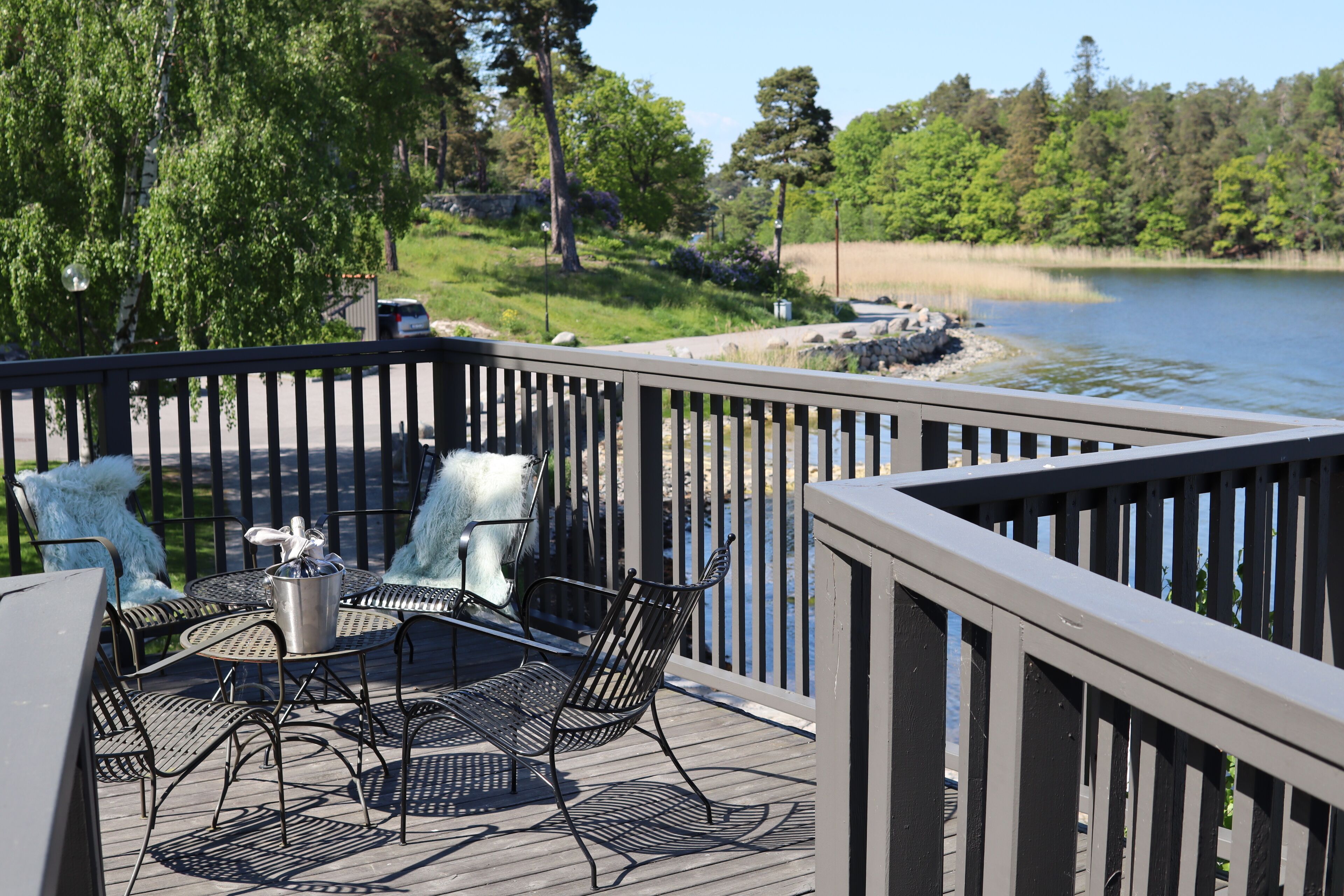 Eine Terrasse mit Gartenmöbeln, Blick auf einen See und bewaldete Hügel im Hintergrund.