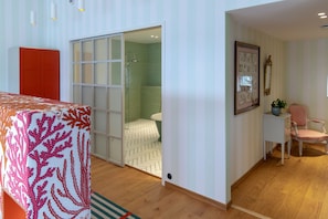 Una habitación con una cama, una puerta corredera hacia la zona de la ducha, una mesita con una planta y una silla.