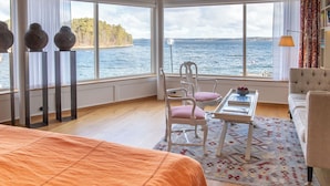 Una habitación con un ventanal grande con vista a un cuerpo de agua, una cama, una mesita con una bandeja y dos sillas.
