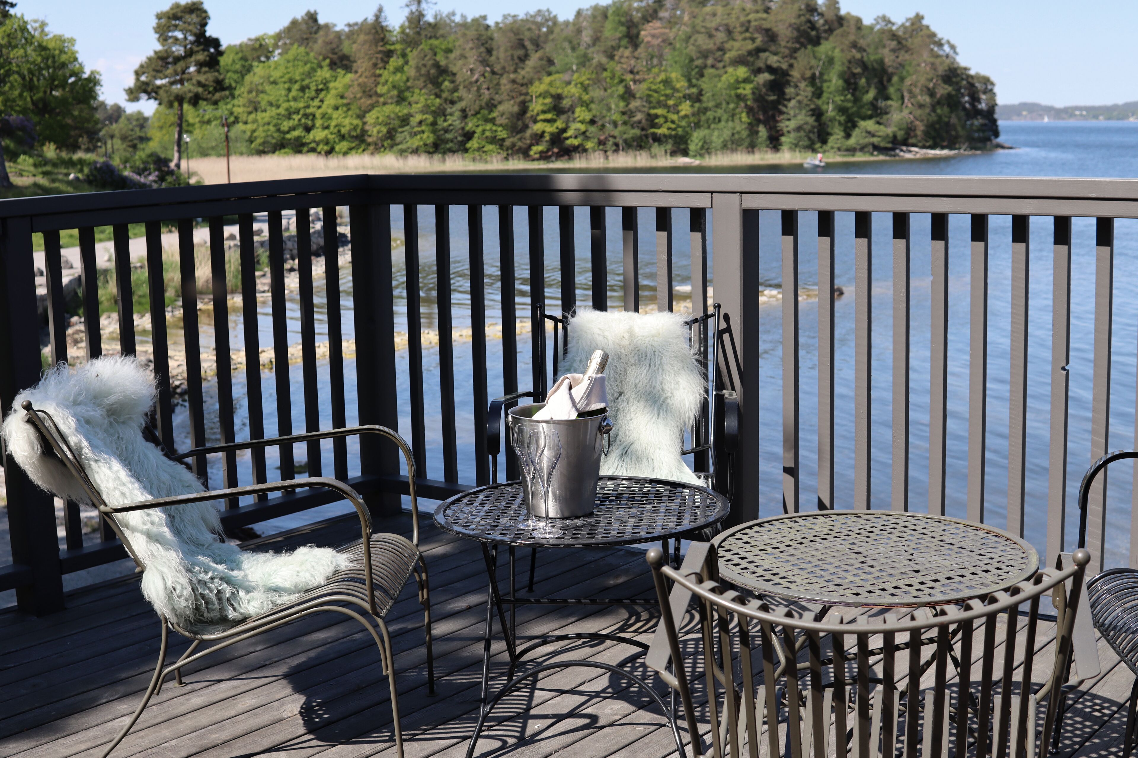 Une terrasse dotée de chaises et d’une table en métal, offrant une vue sur une étendue d’eau et une zone boisée.
