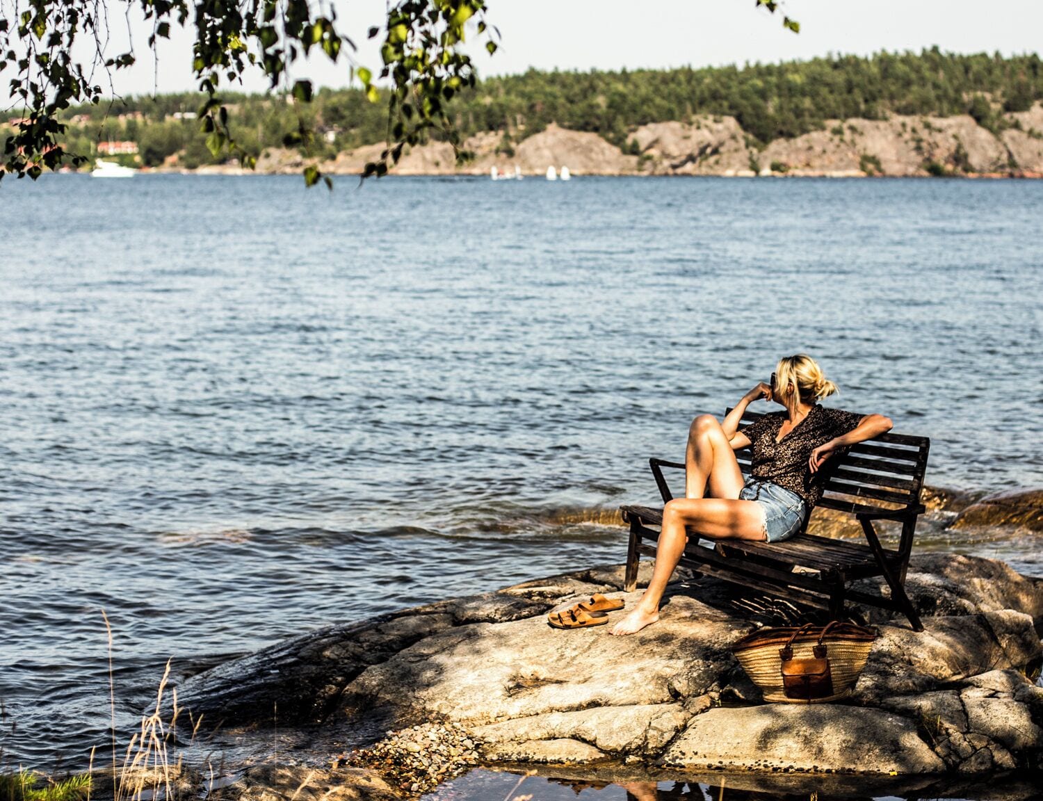 A person sitting on a bench by a body of water with a rocky shore in the background.