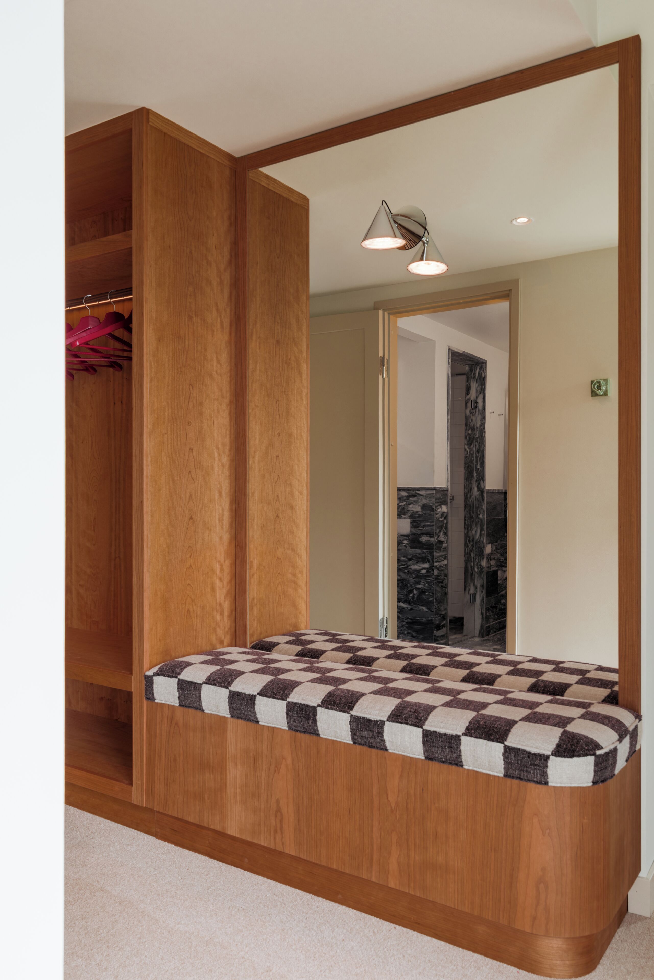 Un dormitorio con un armario de madera, un colchón a cuadros y un espejo.