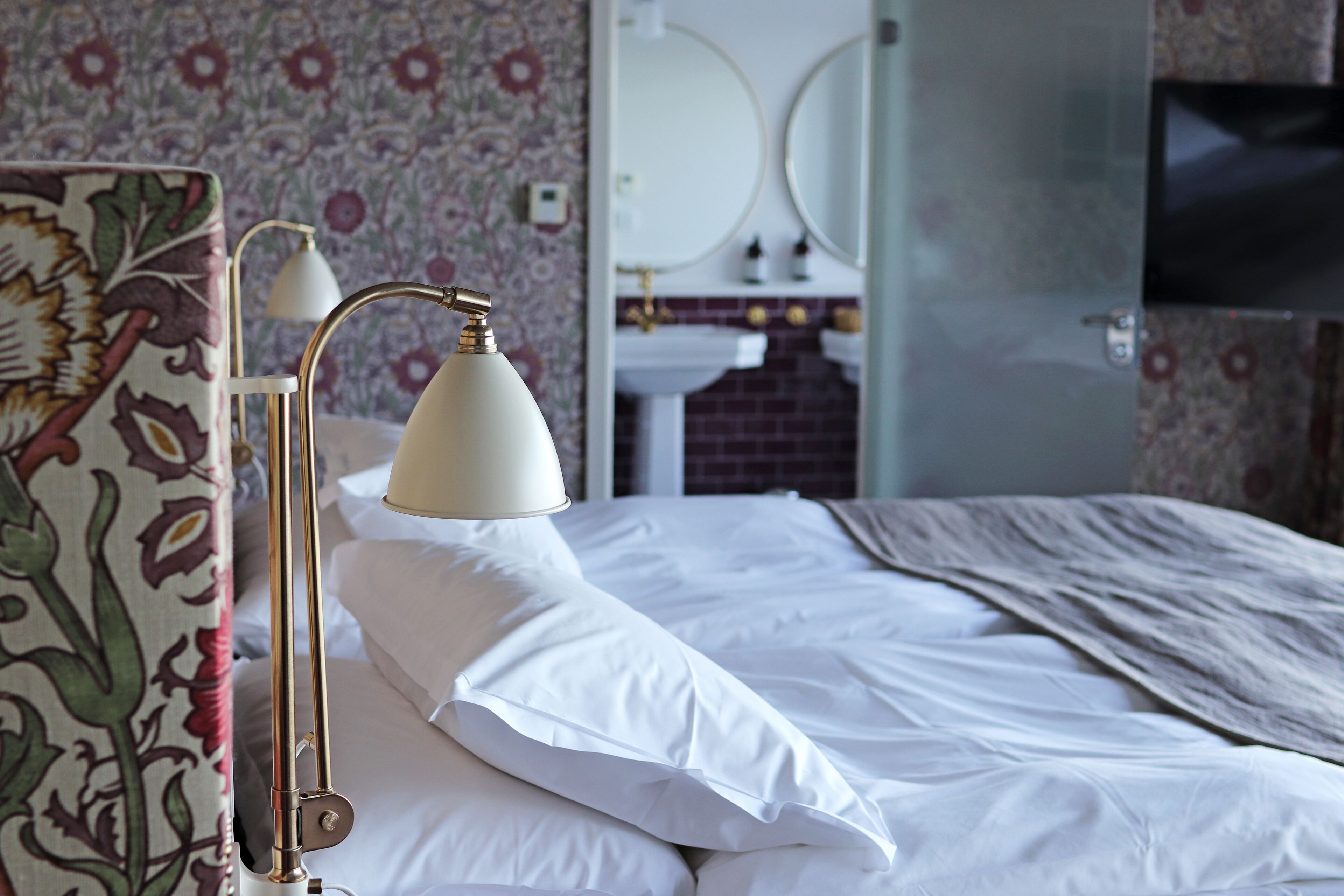 Ein ordentlich bezogenes Bett mit weißen Leinen und einer Lampe daneben.