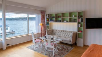 Een woonkamer met uitzicht op een meer, een bank, een salontafel, stoelen, een boekenkast en een televisie.