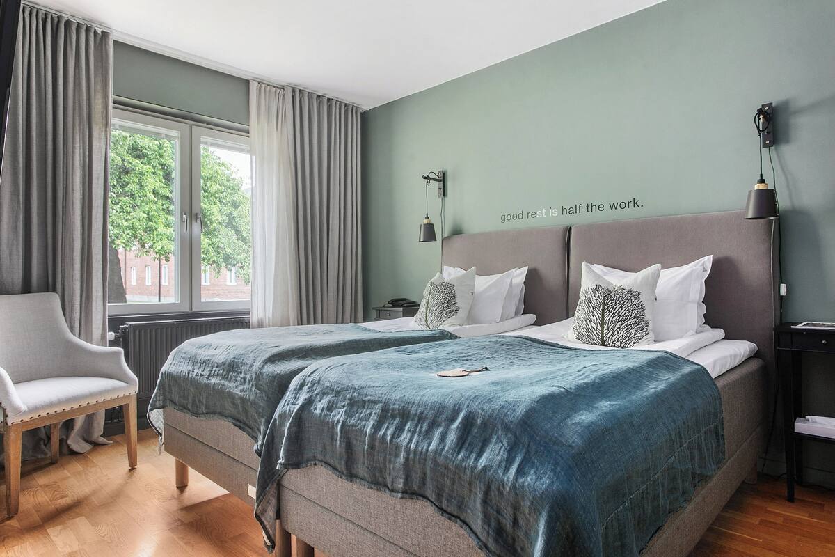 A double bed with a grey headboard, two pillows, and a blue blanket.
