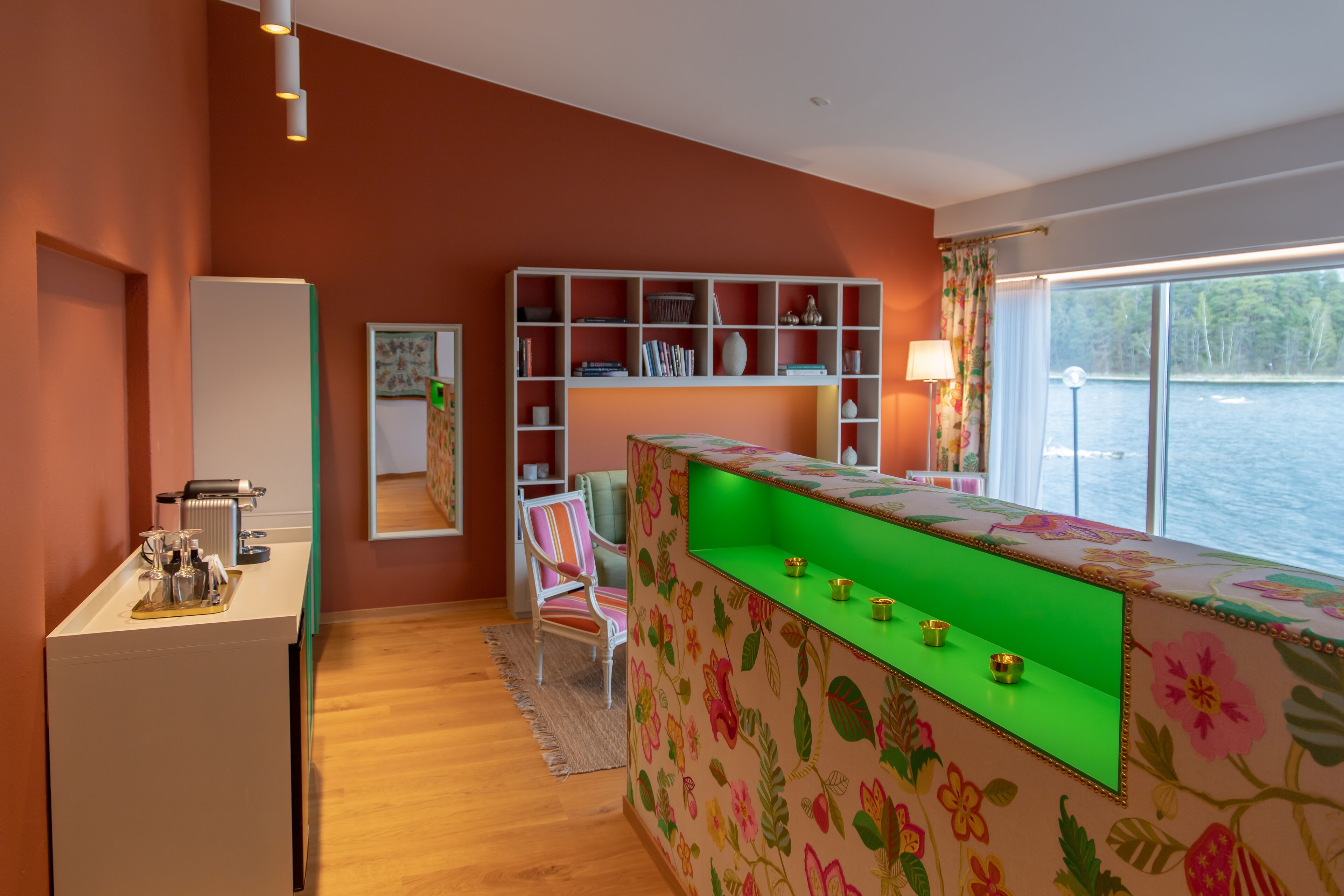 A modern kitchen with a wooden countertop, a built-in bookshelf, and a large window overlooking a body of water.