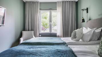 A hotel room with a bed, a chair, a window with curtains, and a wall-mounted lamp.