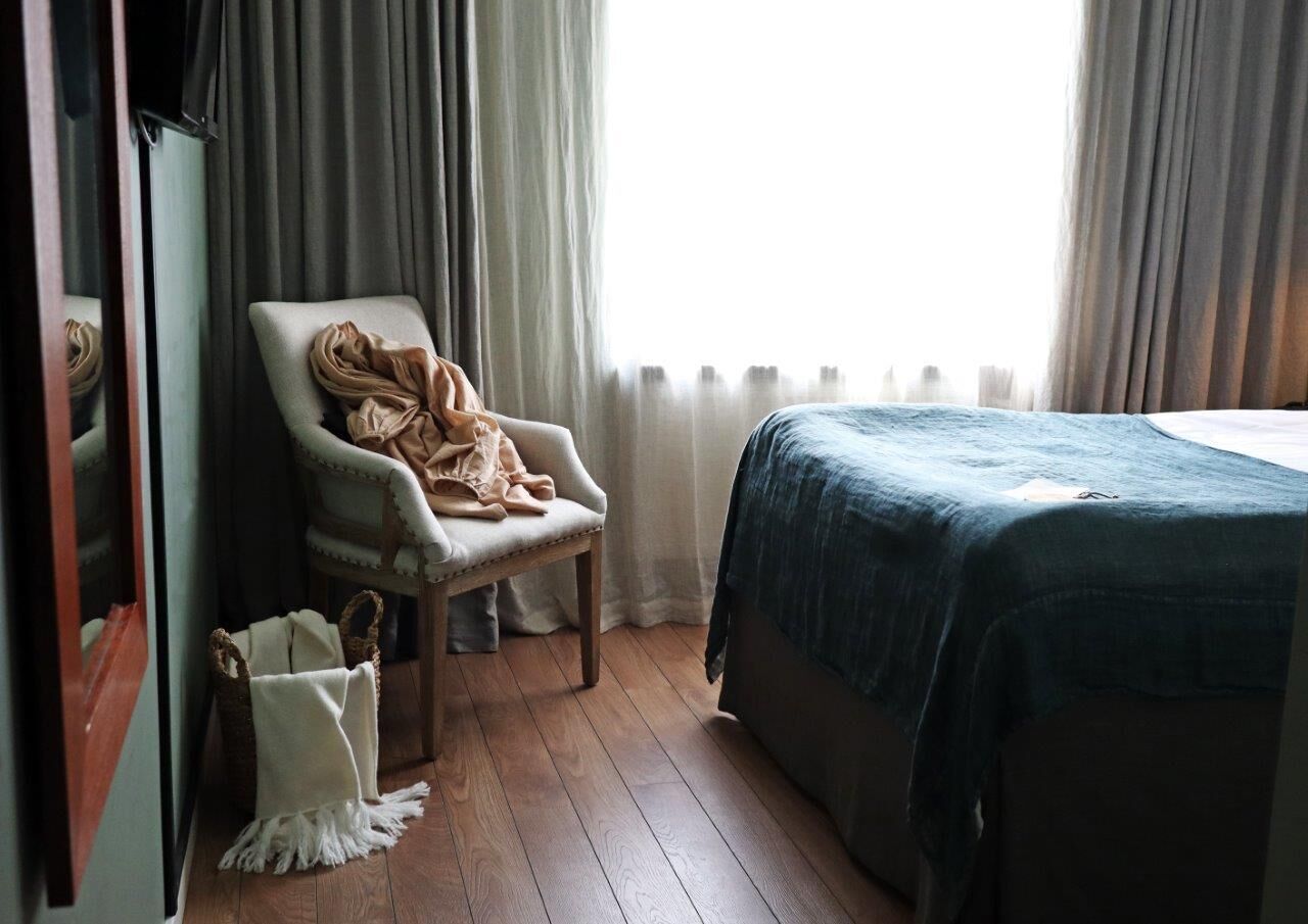 Una habitación con cama, una silla y un ventanal con cortinas.