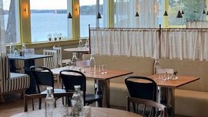 Un restaurante con mesas preparadas para comer, vista al agua y un área de estar con vistas.