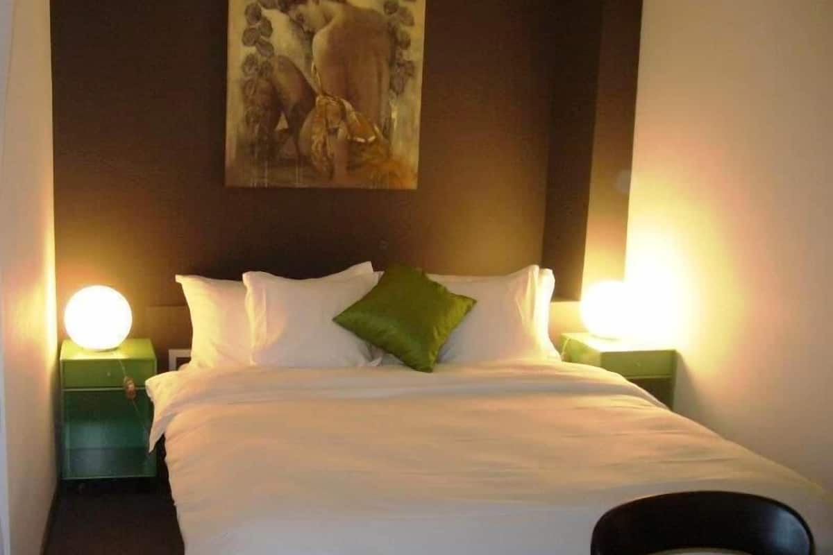 A neatly made bed with white linens and a green pillow, flanked by two bedside lamps.