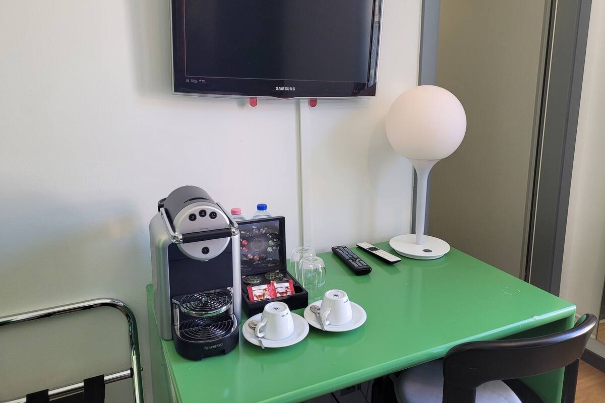 A green table with a coffee machine, two cups, a remote control, and a lamp.