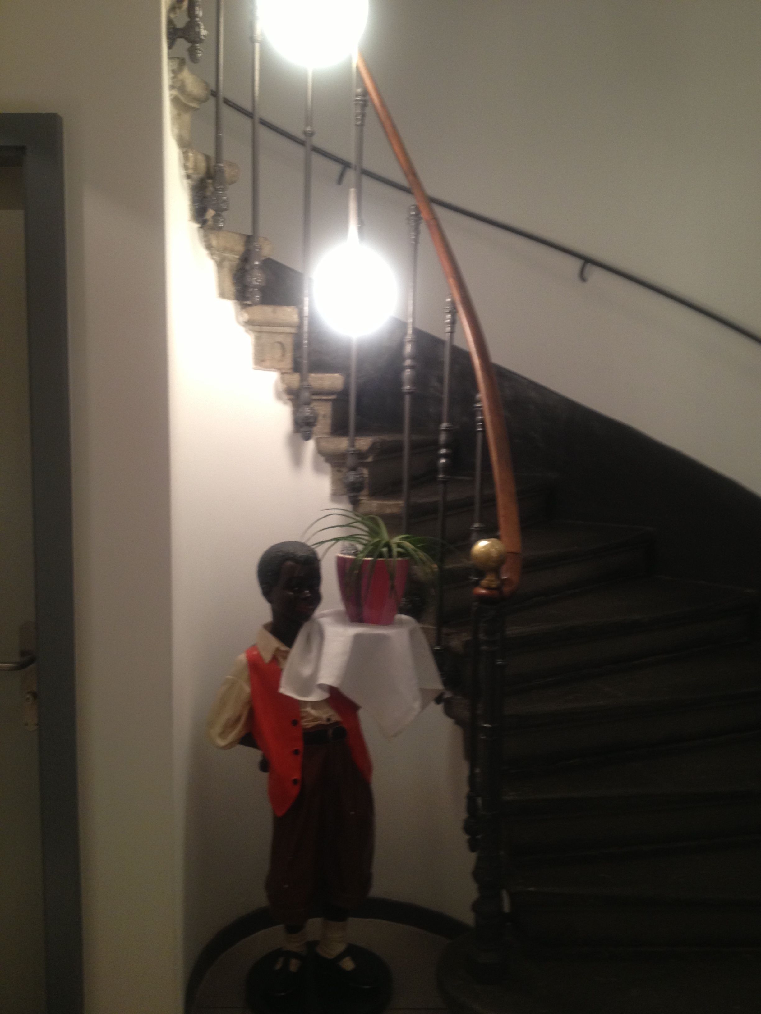 Un escalier muni d’une rampe, un luminaire et un mannequin vêtu d’une veste rouge et d’un pantalon marron.