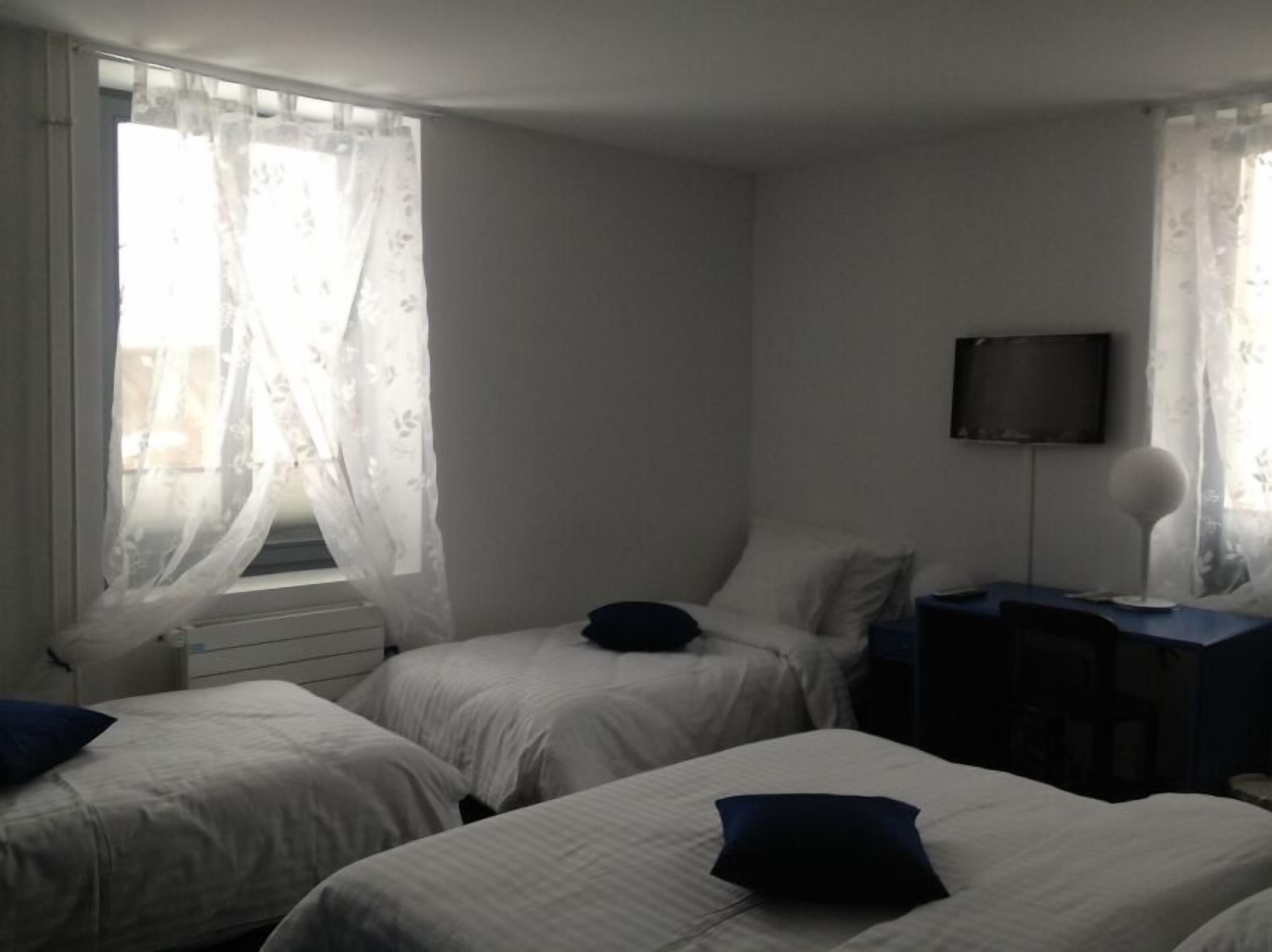 A room with two single beds, a TV on a stand, and a window with sheer curtains.