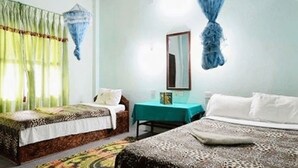 A bedroom with two beds, a small table, and a mirror. - Chitwan Gaida Lodge (Sauraha)