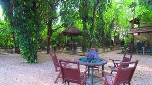 An outdoor seating area with a round table and four chairs, surrounded by trees and a thatched-roof structure. - Chitwan Gaida Lodge (Sauraha)