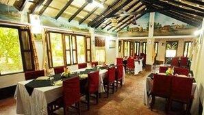 A dining area with multiple tables and chairs, large windows, and a rustic ceiling. - Chitwan Gaida Lodge (Sauraha)