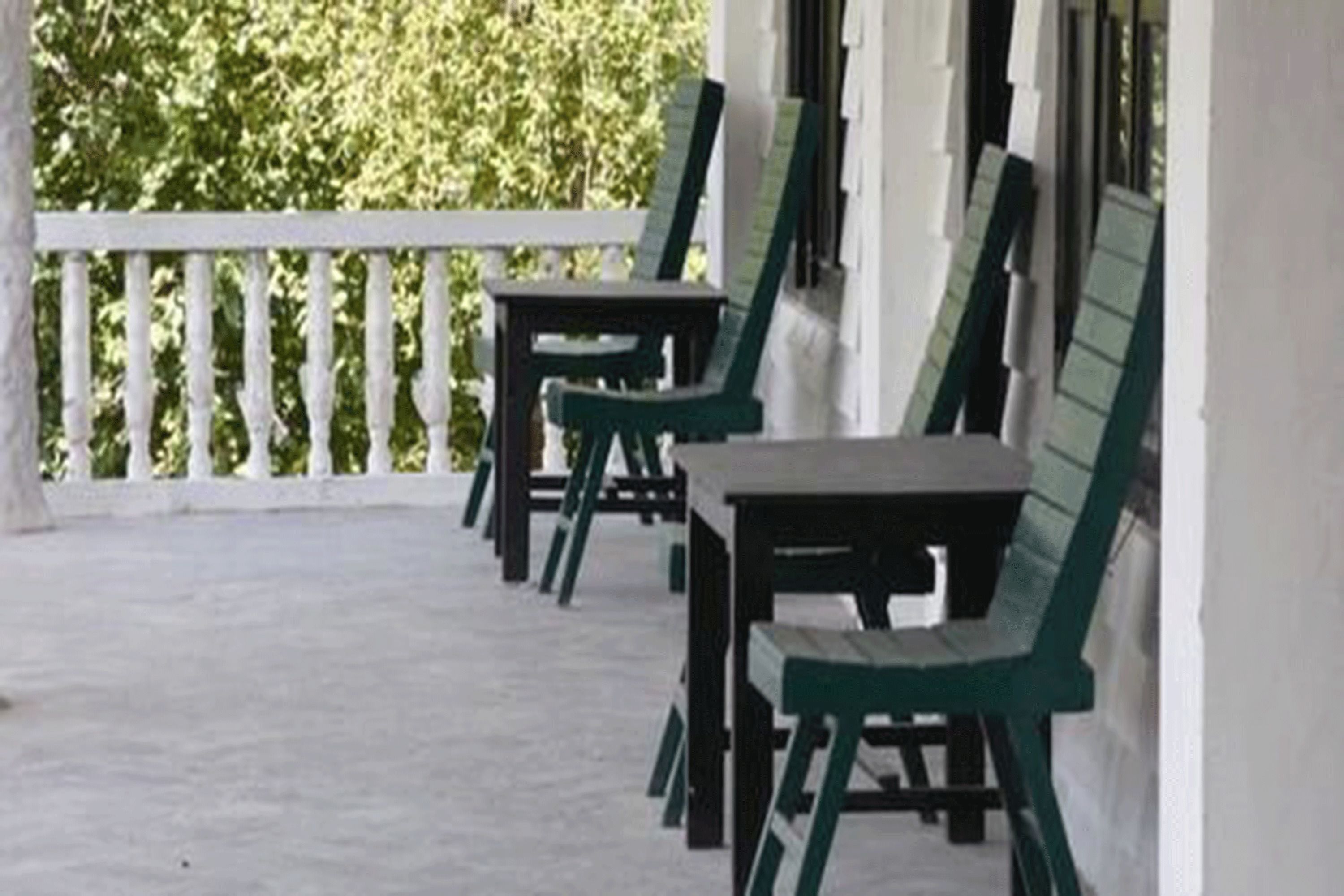 A covered outdoor area with a white railing, green chairs, and tables.