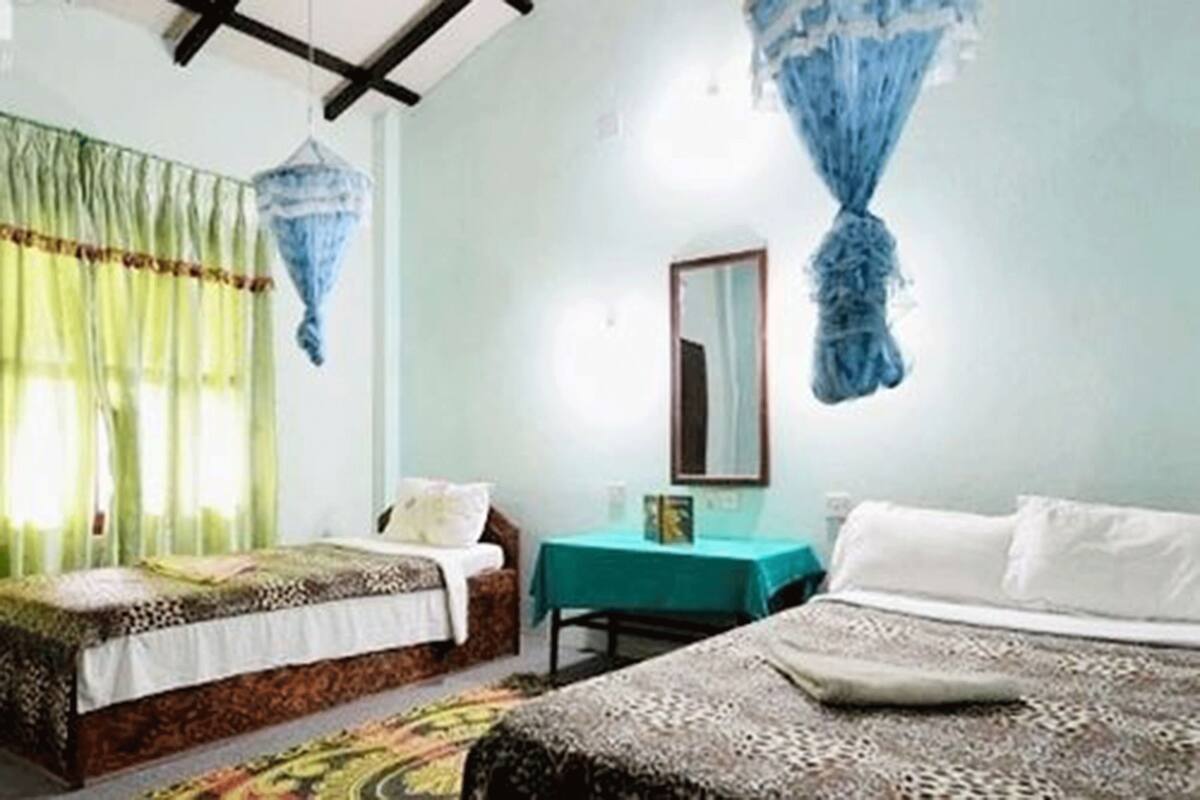 Ein Zimmer mit zwei Betten, einem Tisch, einem Spiegel und einem blauen, hängenden Baldachin.