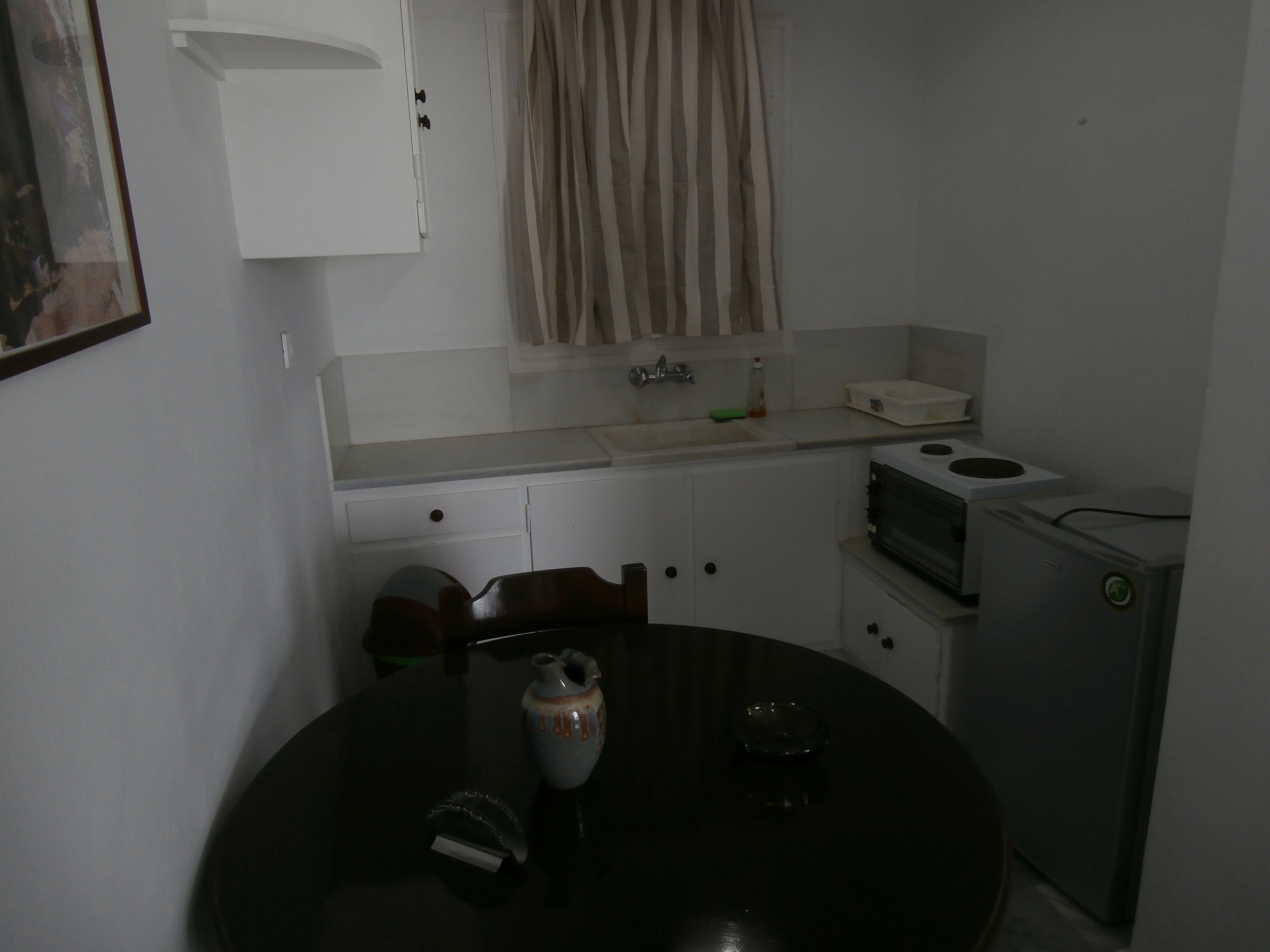 Una cocina compacta con una mesa redonda, un refrigerador pequeño, un microondas y un lavamanos.