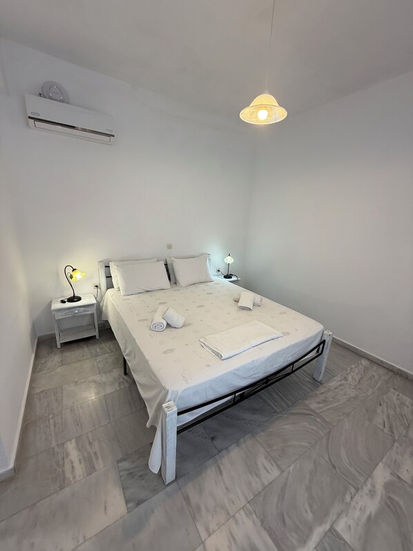 A minimalist bedroom with a bed, bedside lamps, a wall clock, and an air conditioning unit.