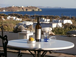A table with a bottle of wine, a glass, and a lemon on a terrace overlooking a coastal landscape with white buildings and a view of the sea.