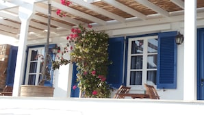 A covered outdoor area with a wooden ceiling, a potted plant with pink flowers, and a wooden bench. - Galini Bungalows (Tinos)