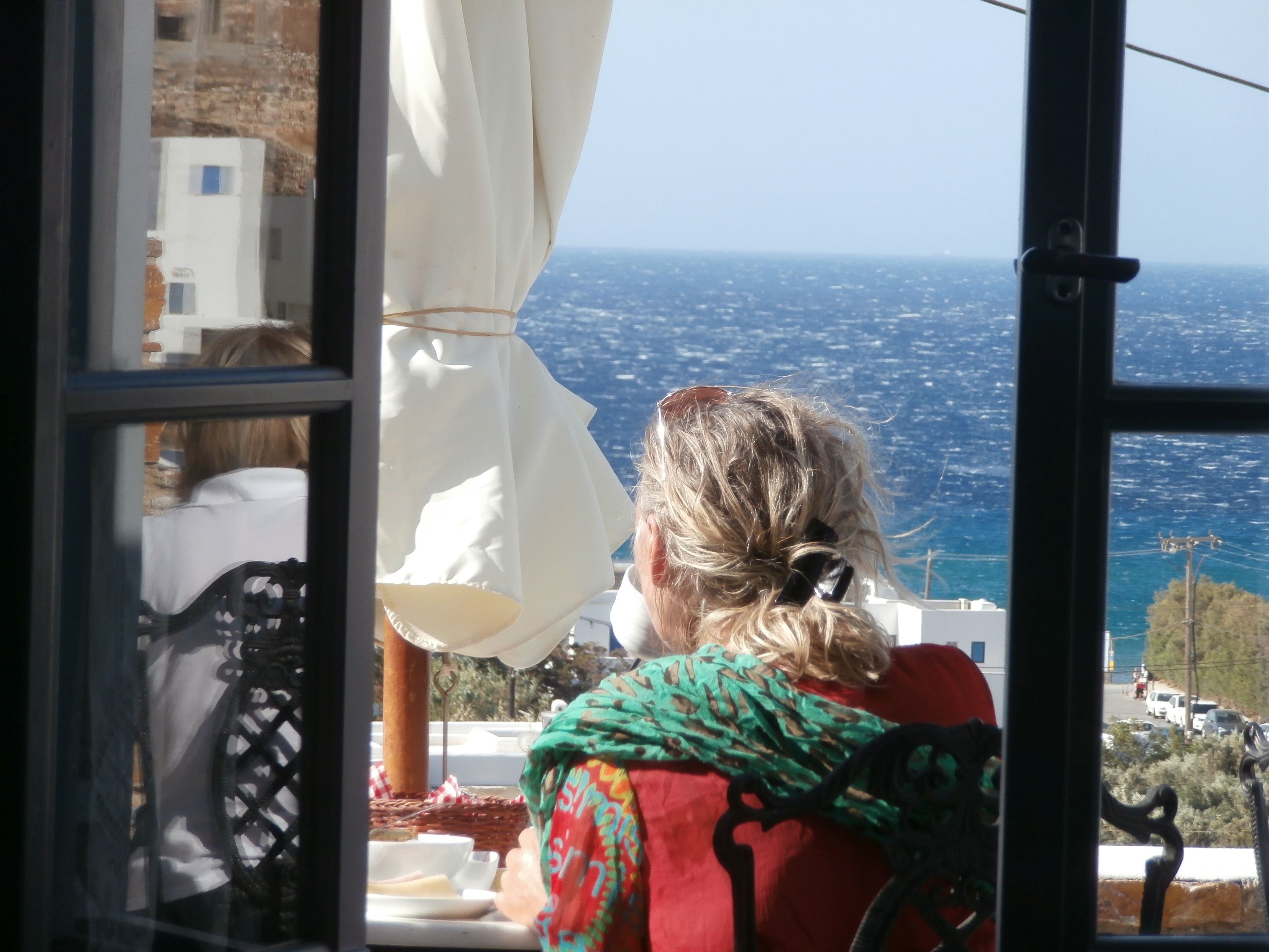 Vista al mar desde una ventana, con una mesa y sillas adentro.